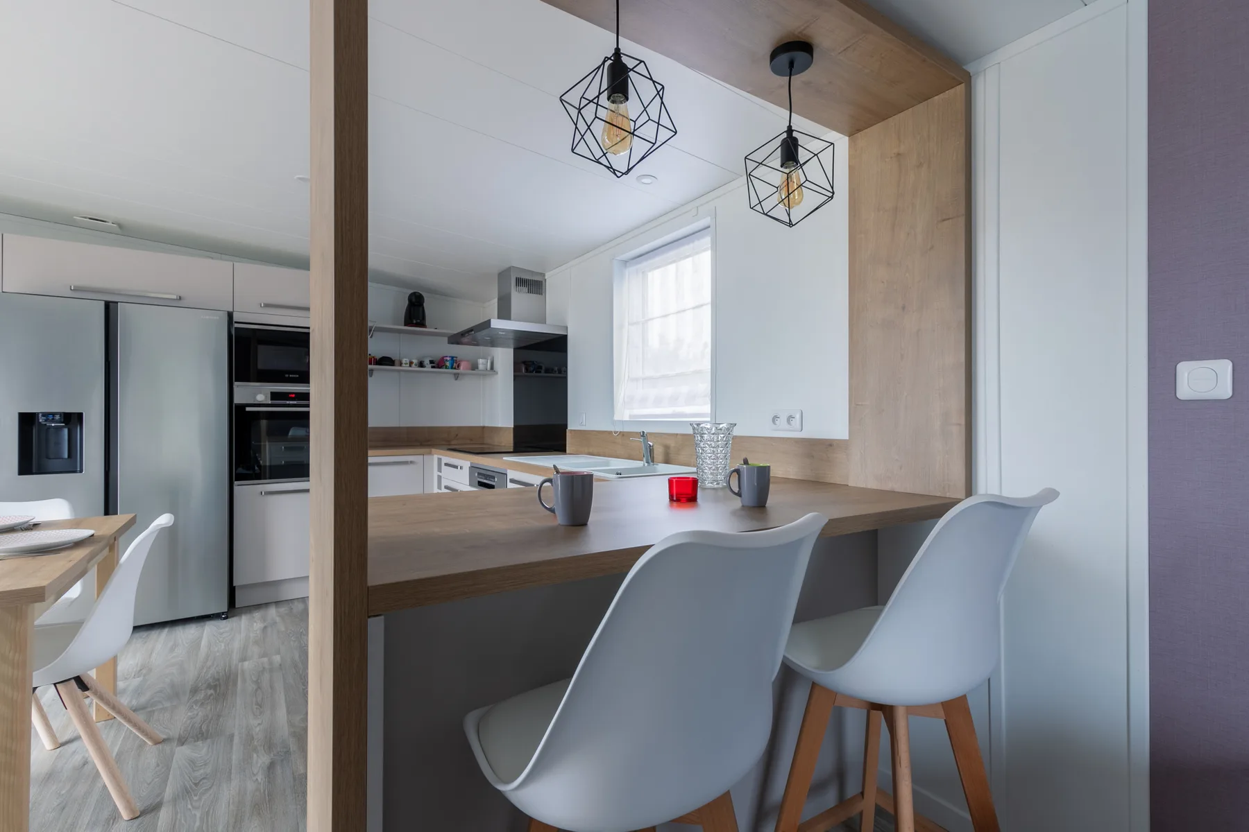 A modern kitchen with a counter and seating beneath pendant lights.