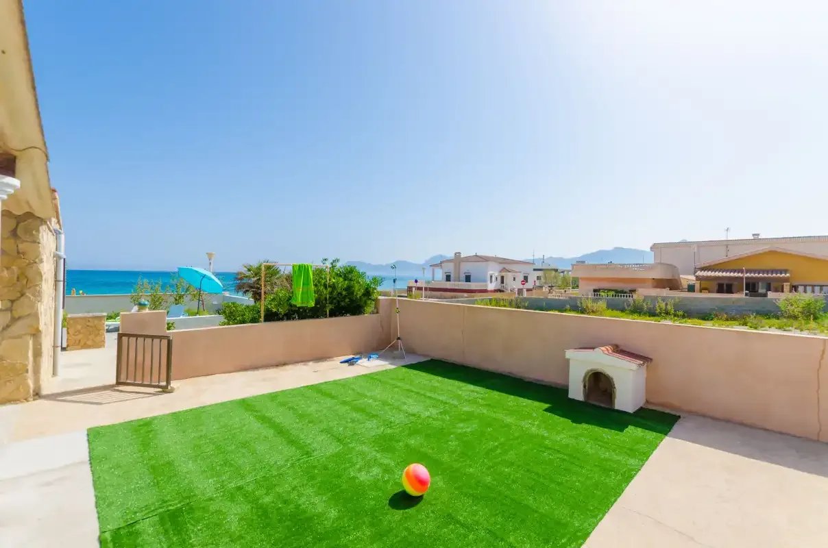 A sunny rooftop terrace has a patch of green turf, a ball, and views of the sea.