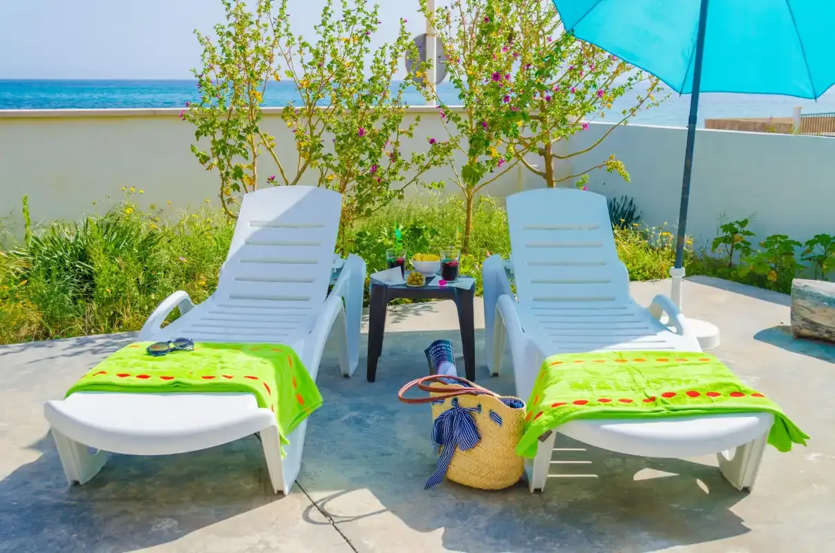 An outdoor patio with two lounge chairs beside a turquoise umbrella.