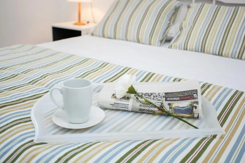 A striped bedspread with a tray holding a cup and a rolled newspaper.