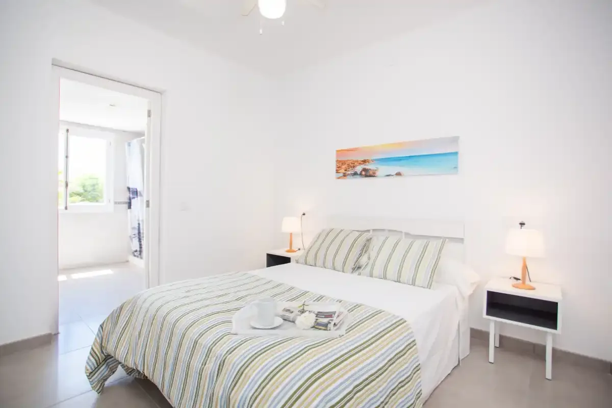 A bright bedroom with a neatly made bed and striped bedding.