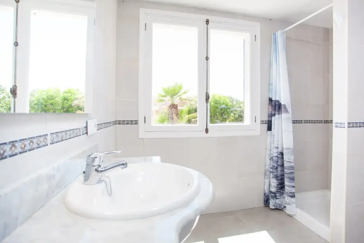 A bright bathroom with a sink, window, and shower.