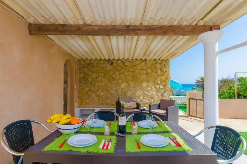 A covered outdoor dining area with a table set beside a stone wall.