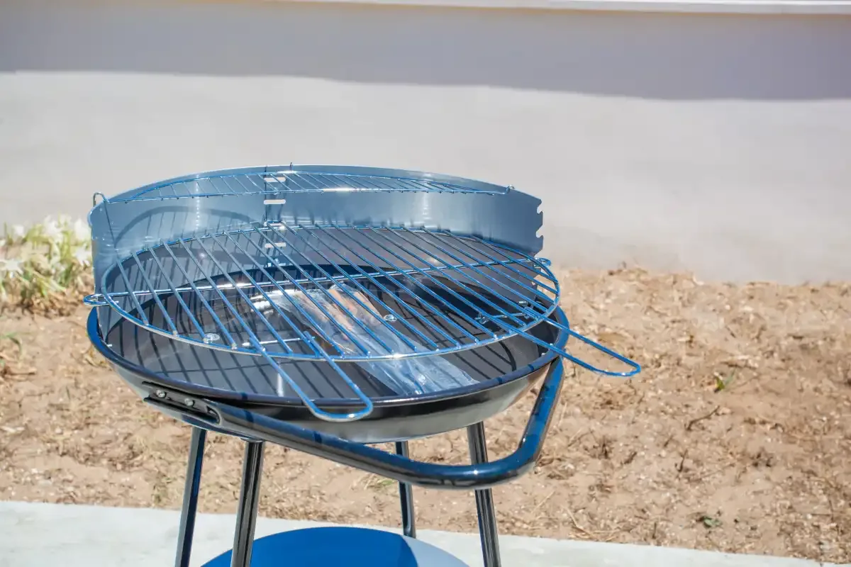 A round metal barbecue grill stands outdoors on a paved surface.