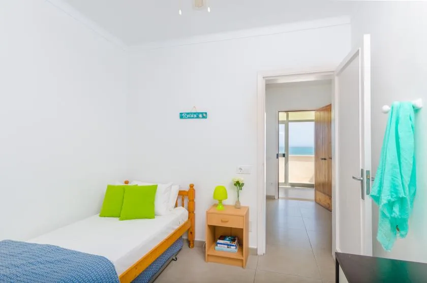 A bright bedroom with a single bed and an open doorway leading toward the beach.