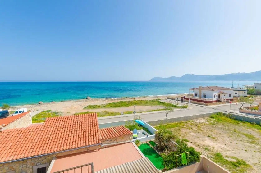 Coastal residential scene with turquoise sea, sandy shore, and low buildings.