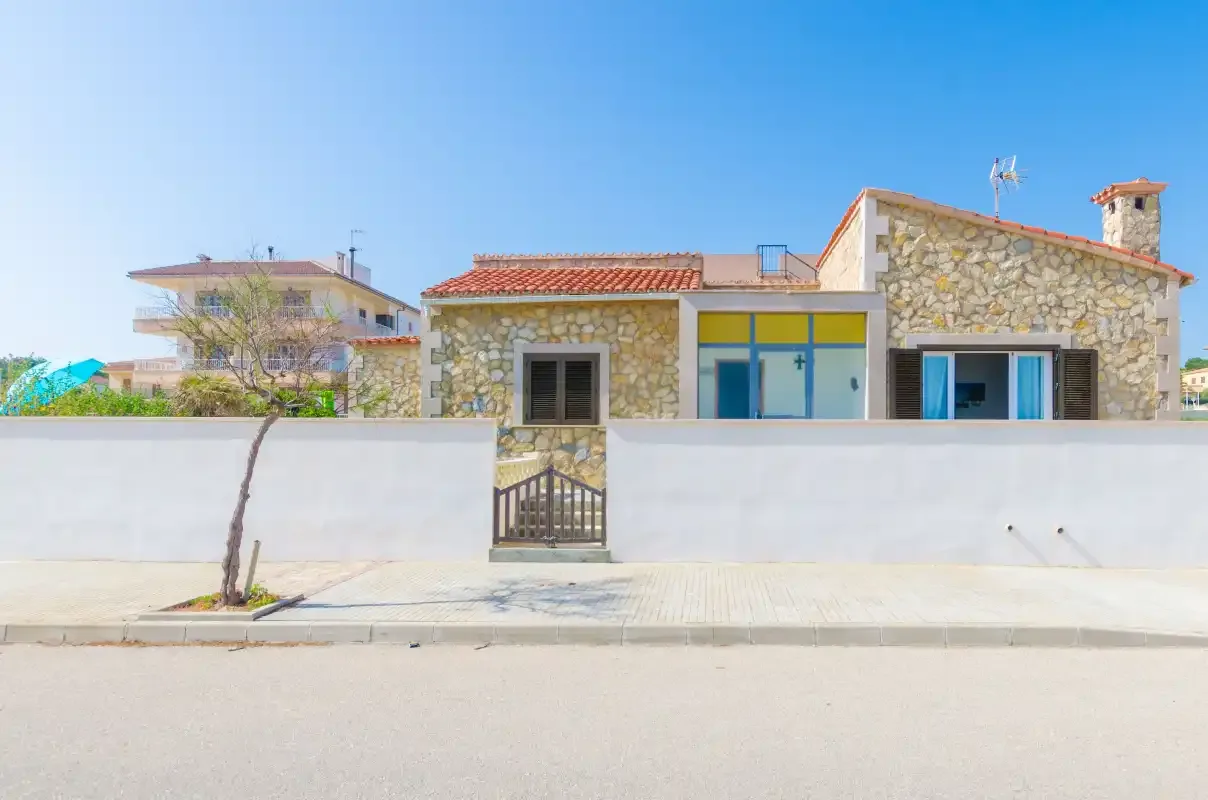 A stone house stands behind a low white wall along a quiet street.
