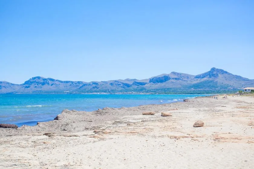 A sandy shoreline borders turquoise water, with mountains across the bay.
