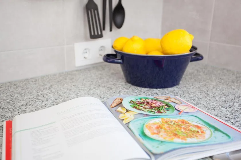 A kitchen countertop holds a bowl of lemons beside an open cookbook.