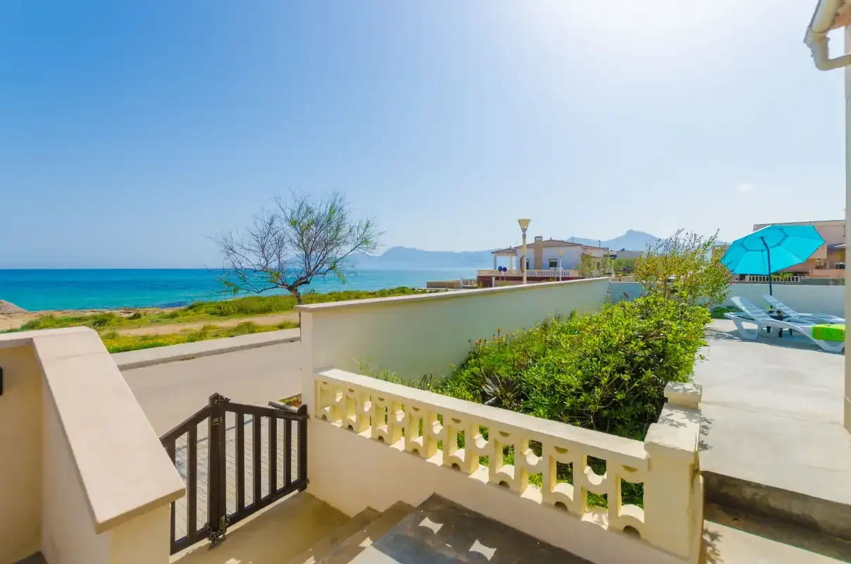 A seaside terrace overlooks the blue water, with outdoor seating nearby.