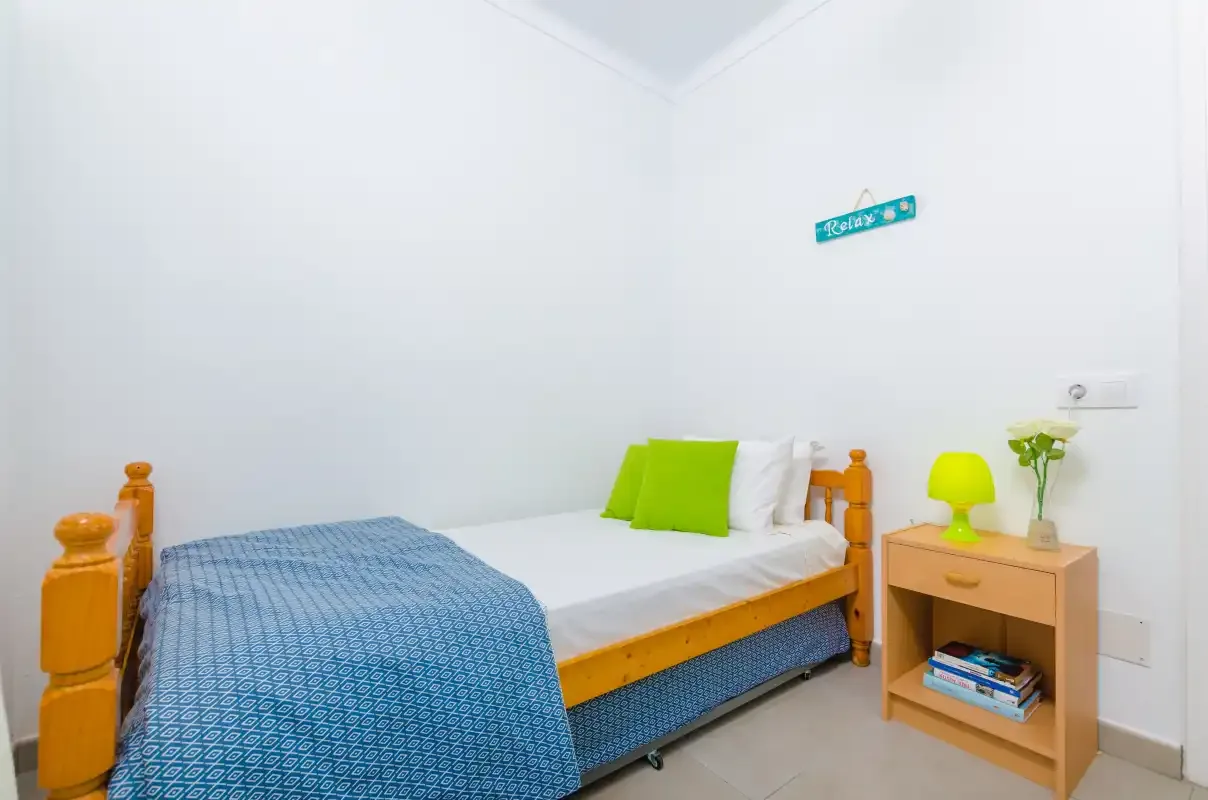 A bright bedroom with a single bed and a small bedside table.
