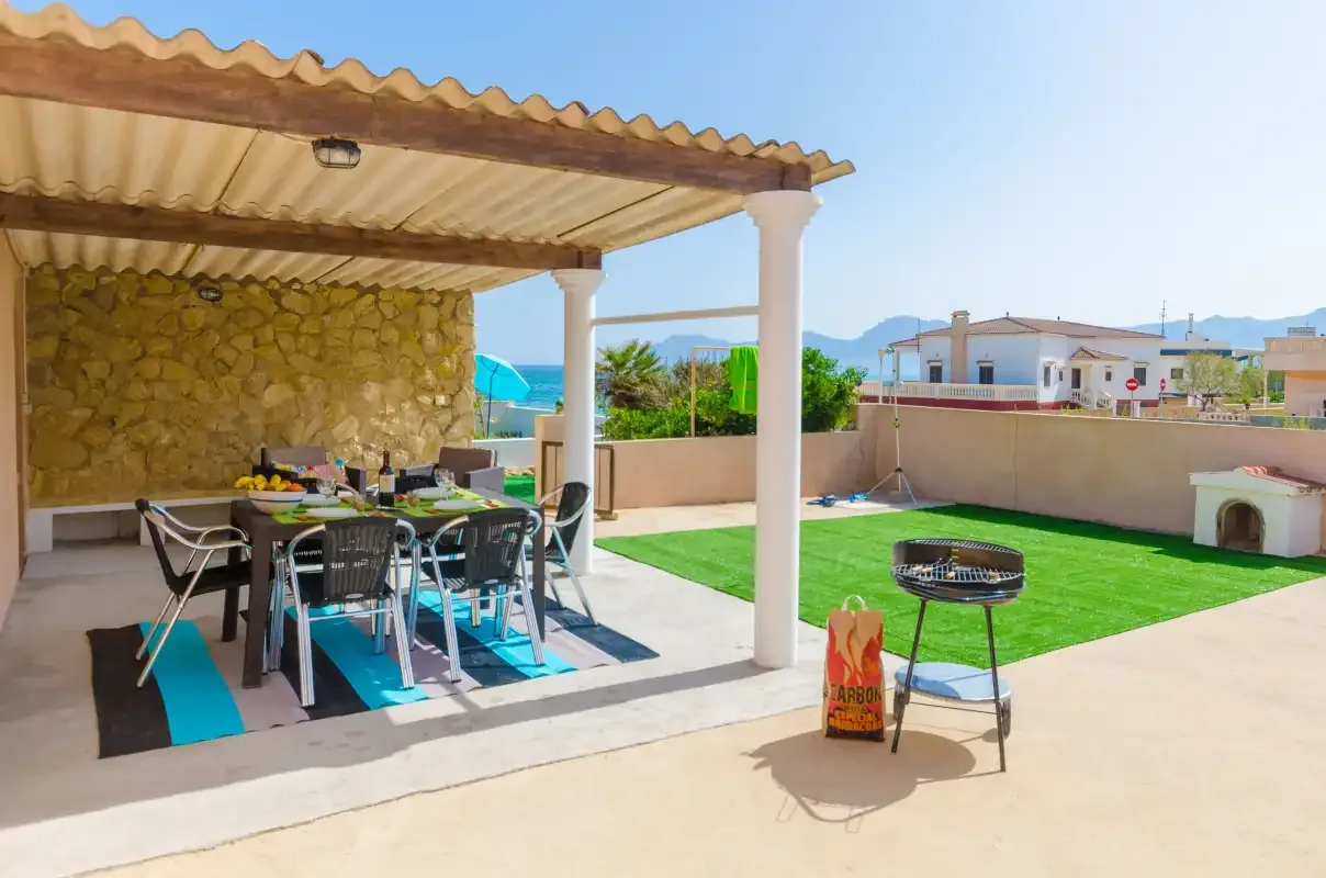 A covered outdoor dining area opens onto a lawn and swimming pool.