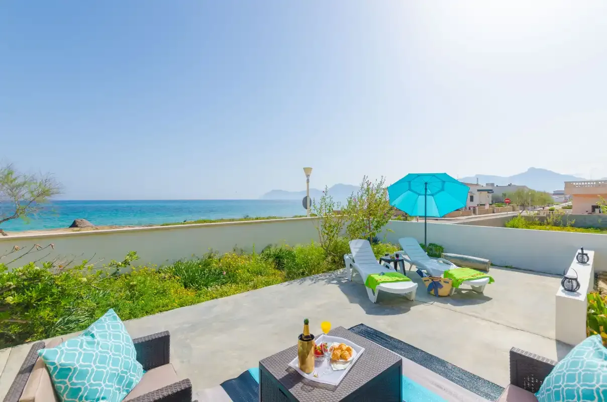 A seaside patio with lounge seating and a blue umbrella overlooks the water.