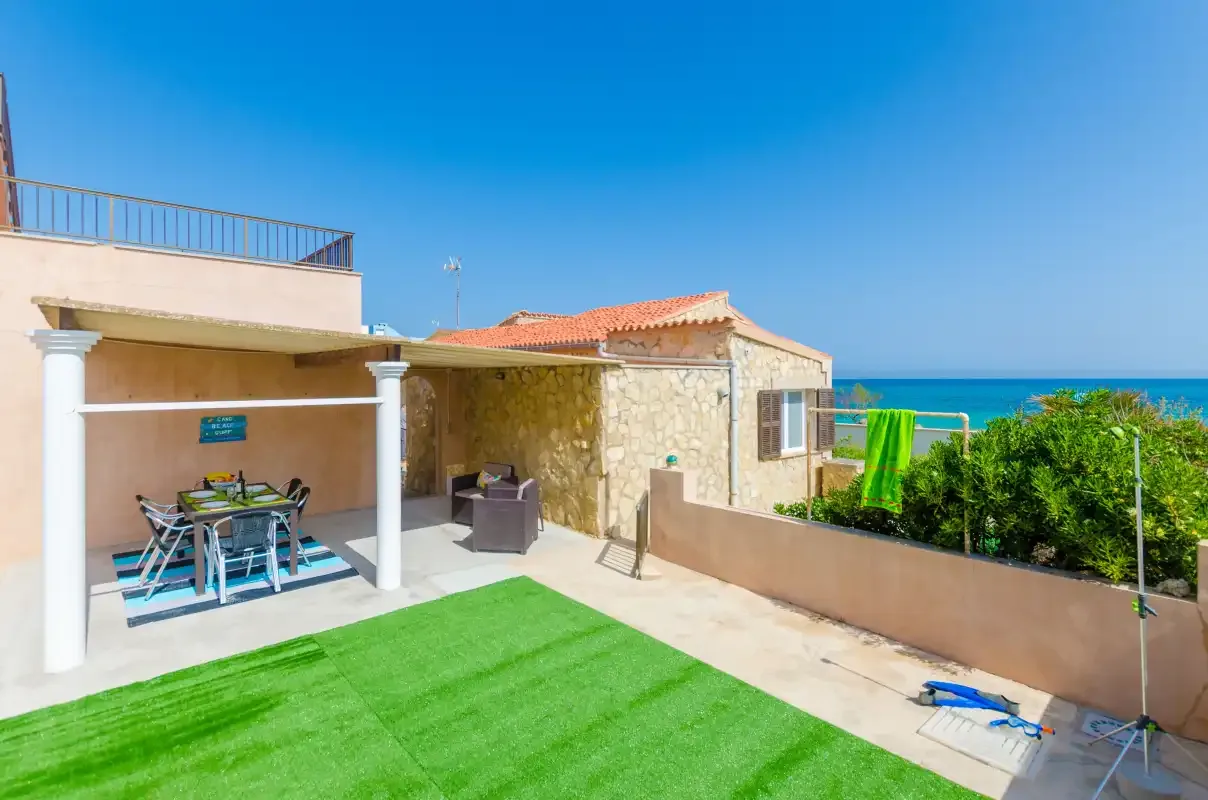 A seaside patio with outdoor seating, green lawn, and a view of the sea.