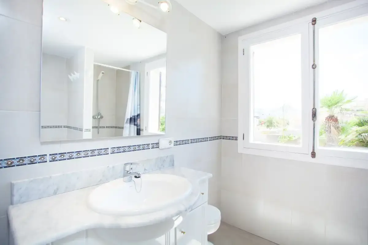 A bright bathroom with a sink, mirror, and window.