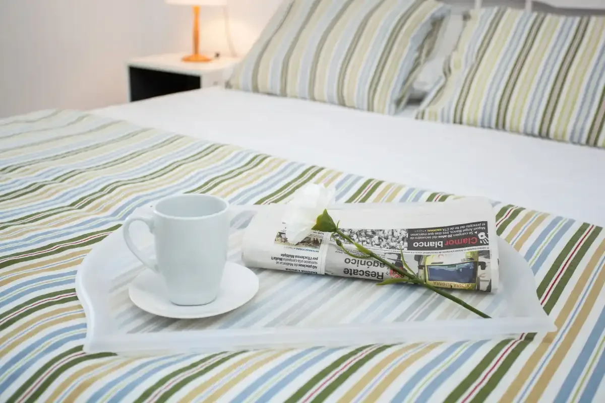 A bedroom with striped bedding and a tray holding a cup and folded newspaper.