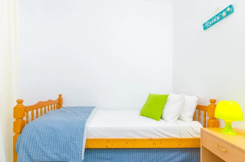 A bedroom with a wooden bed, white bedding, and a green accent pillow.