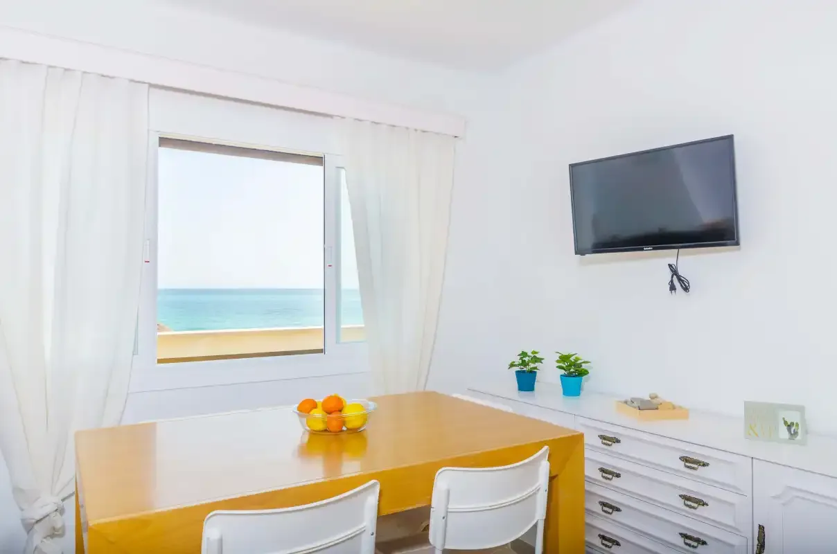 A bright dining area with a wooden table beside a window overlooking the sea.