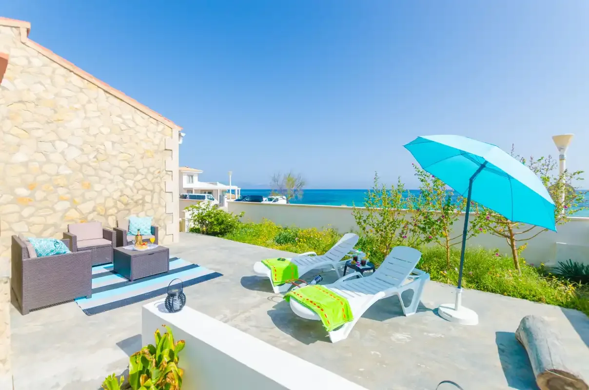 A sunny outdoor patio with lounge seating and a view of the sea.