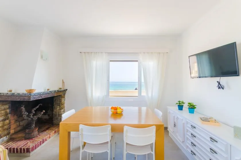A bright dining area has a wooden table beside a window overlooking the sea.