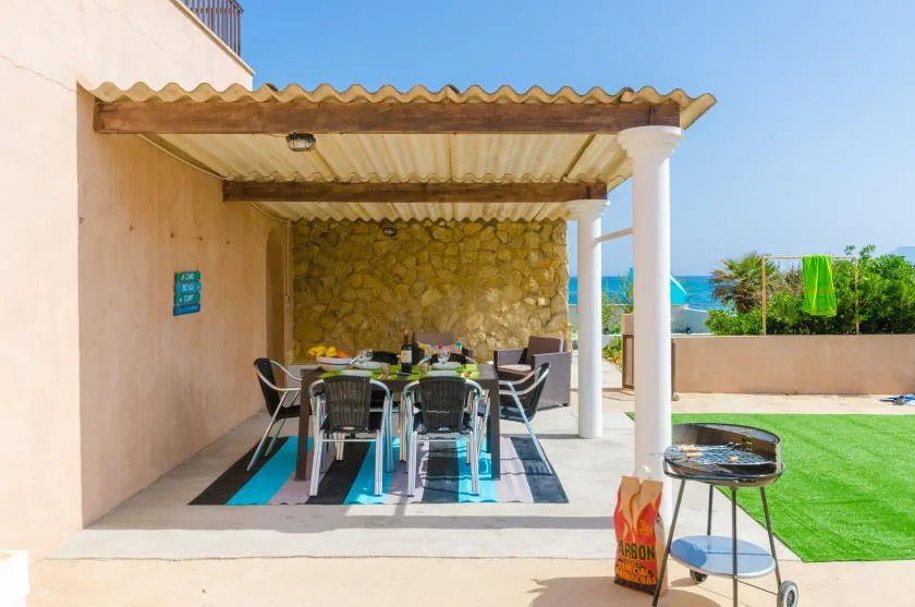 A covered outdoor dining area with a table and chairs beside a green lawn.