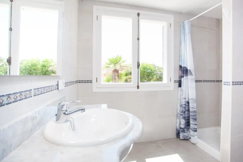 A bright bathroom with a sink, windows, and a shower curtain.
