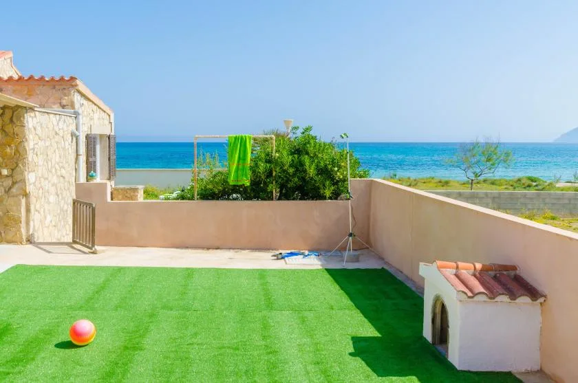 A seaside terrace with a green lawn and blue water beyond the wall.