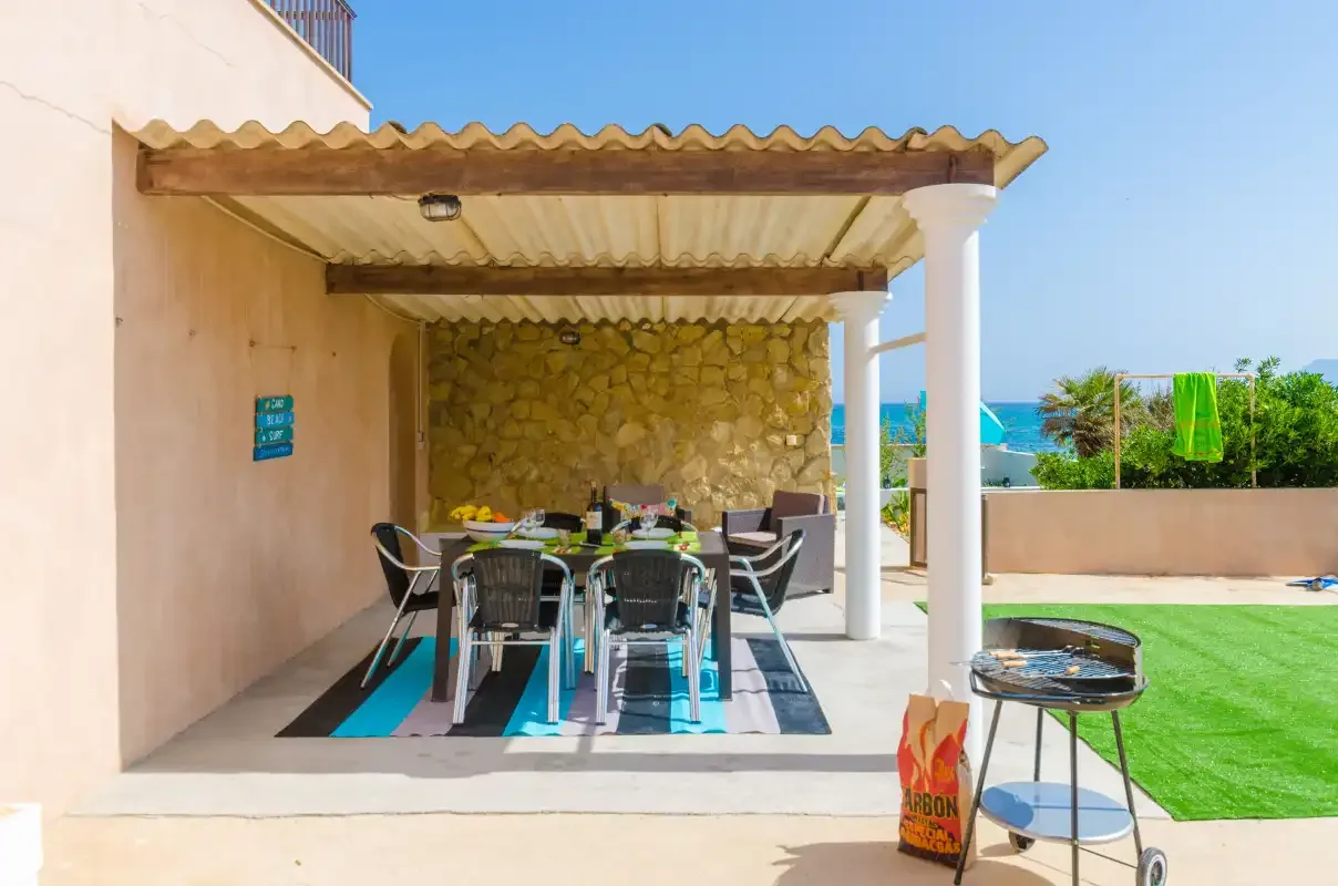 A covered outdoor dining area with a table and chairs beside a lawn.
