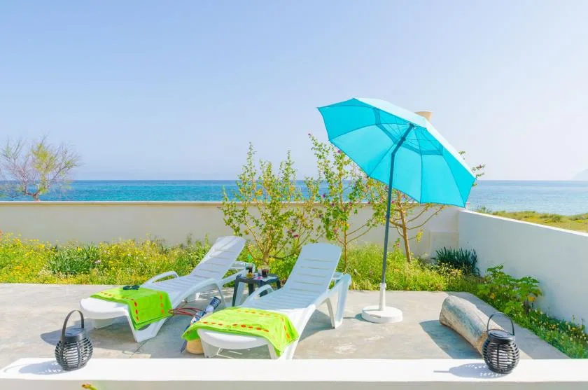 A seaside patio with lounge seating and a bright turquoise umbrella.
