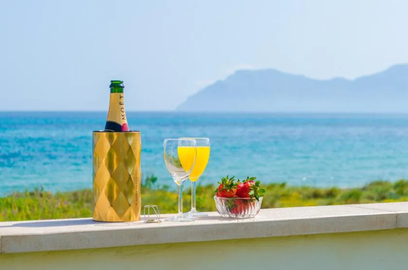 A seaside ledge displays a bottle, drinks, and a small bowl of fruit.