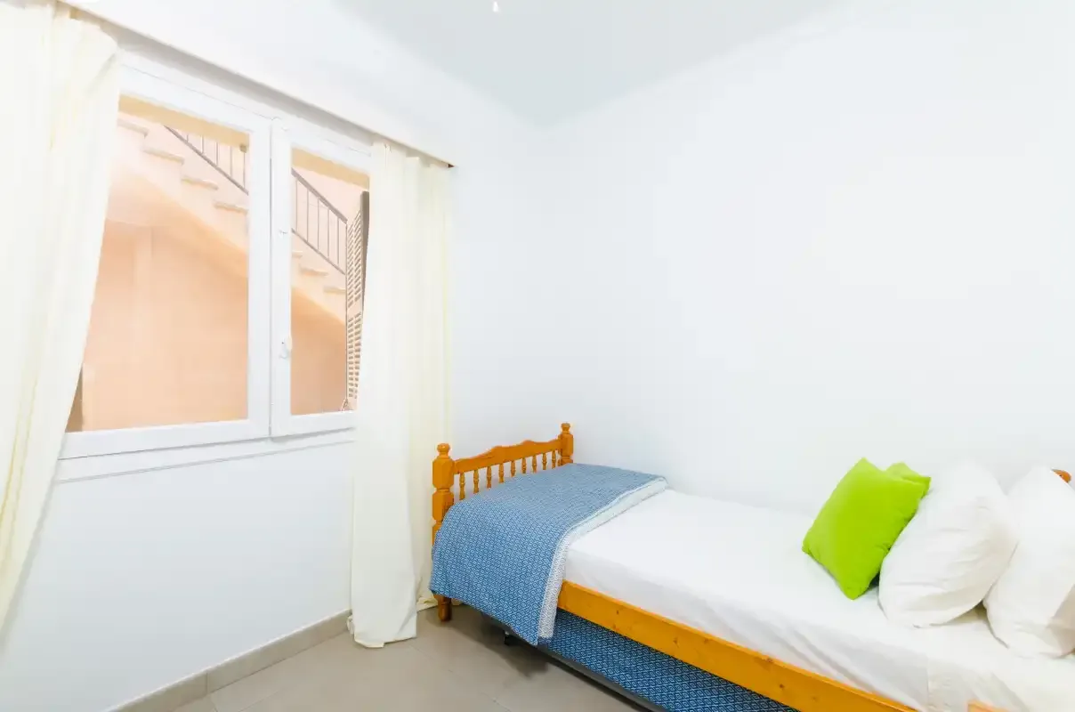 A bright bedroom with a single bed beside a window.