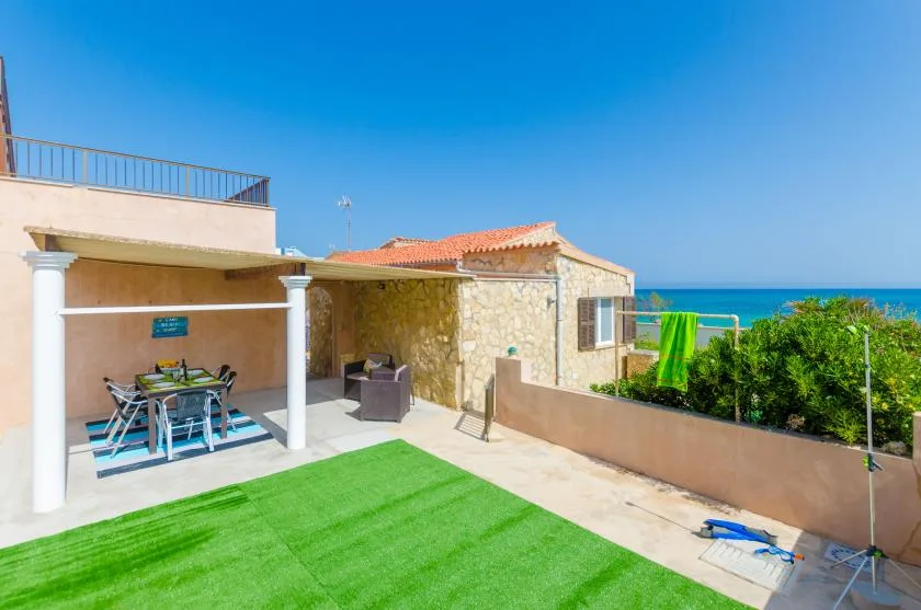 A sunny outdoor patio with a dining table, green lawn, and ocean view.
