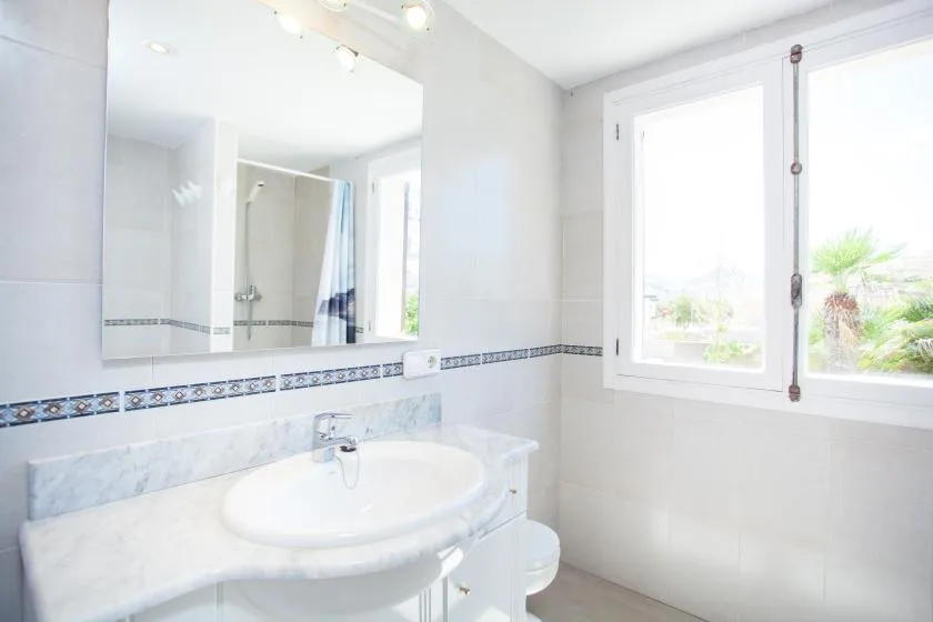 A bright bathroom with a sink, mirror, and large windows.