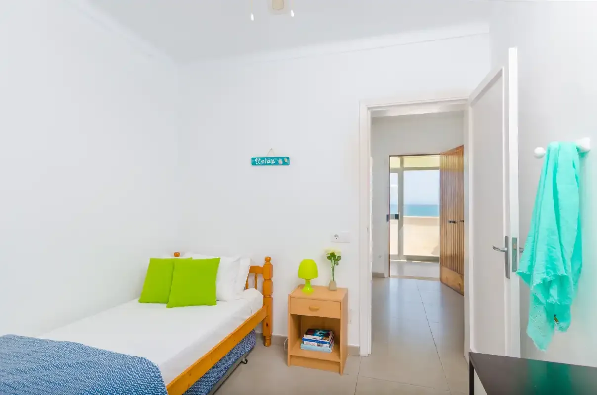A bright bedroom with a single bed and an open doorway to a balcony.