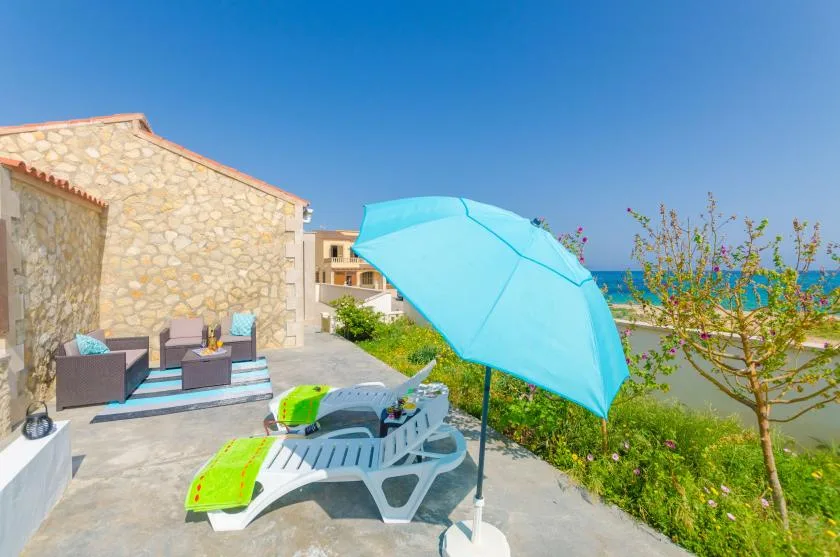 A sunny outdoor patio has lounge seating, sun loungers, and a bright blue umbrella.