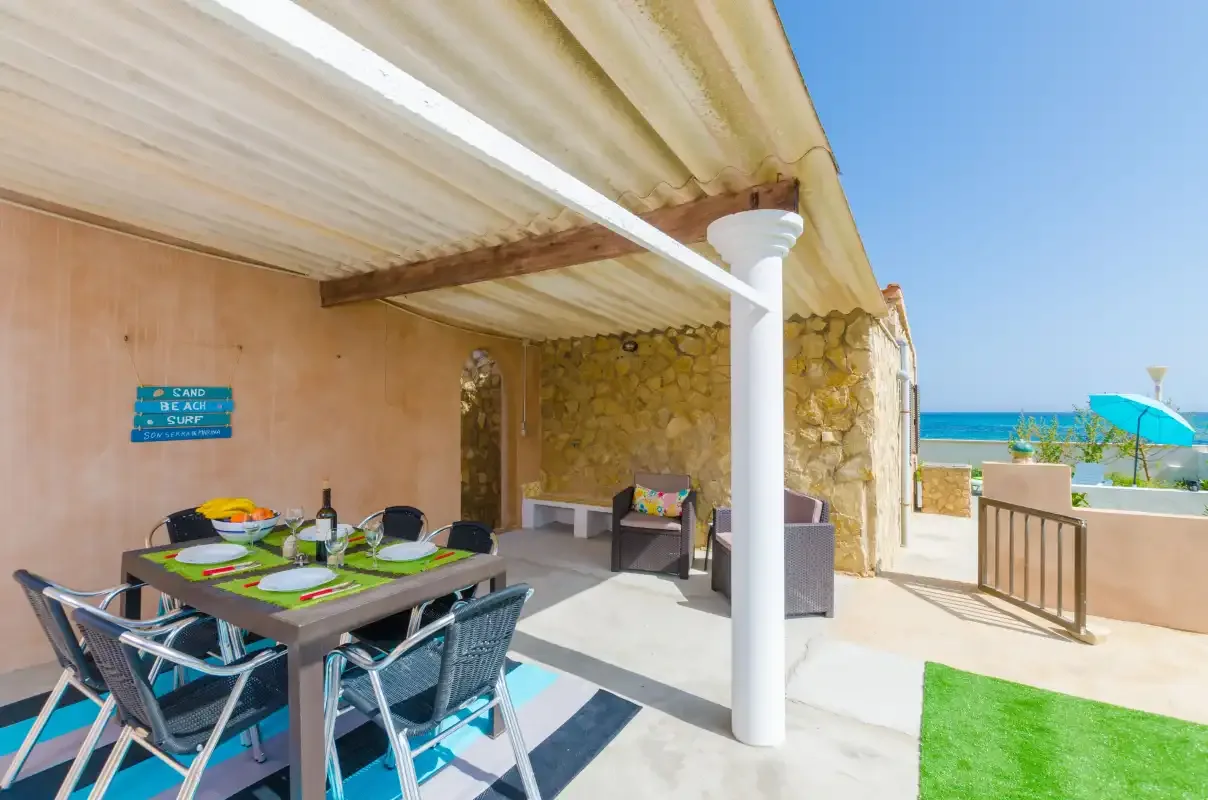 A covered outdoor dining area opens onto a sunny terrace by the sea.