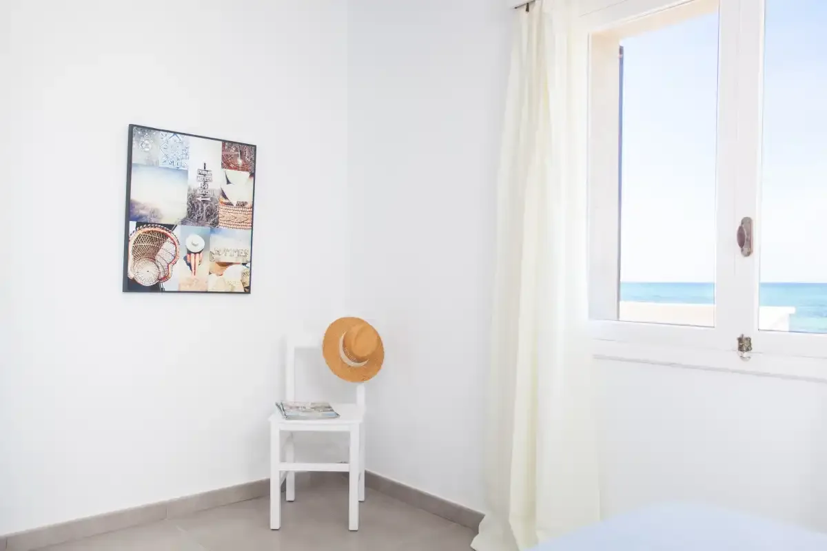 A bright bedroom with a small bedside table and a window overlooking the sea.