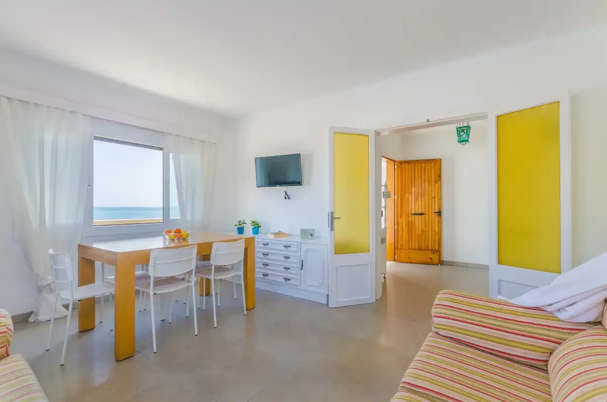 A bright room with a dining table, seating, and a view of the sea.