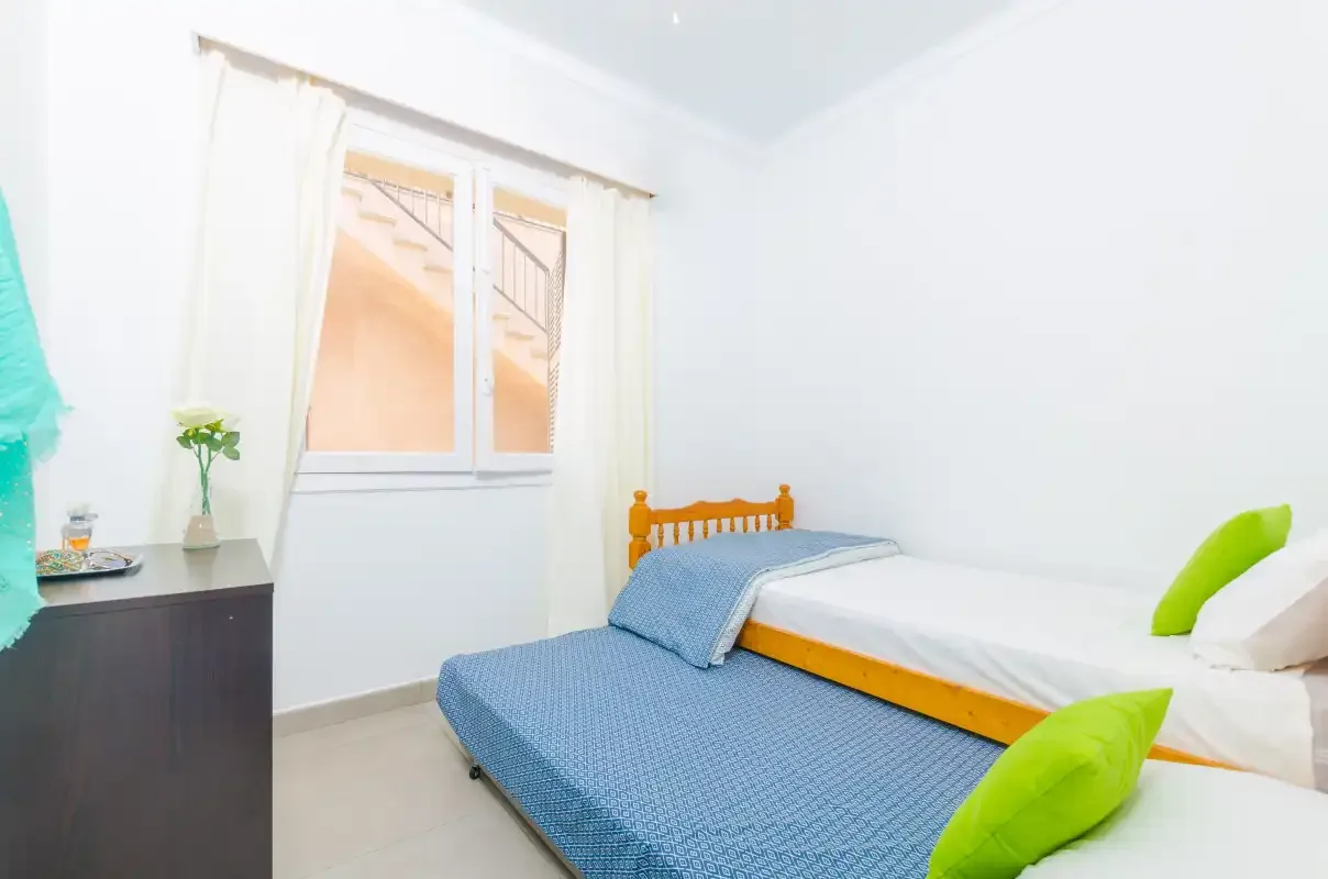 A bright bedroom with a single bed and a blue-covered bed beside it.