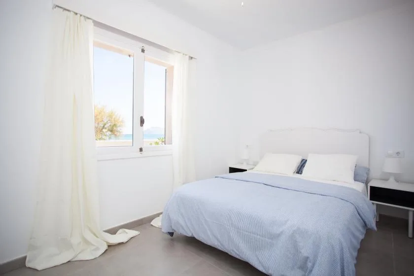 A bright bedroom with a bed beside a window overlooking the water.
