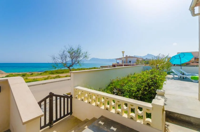 A seaside terrace overlooks the turquoise water, with a low railing and nearby greenery.