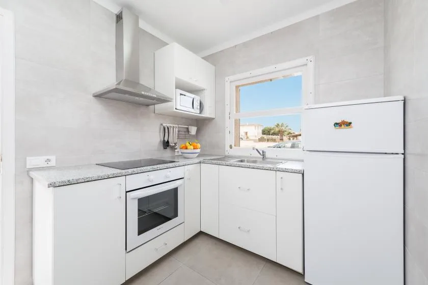 A bright kitchen with white cabinets, a refrigerator, and a window above the sink.