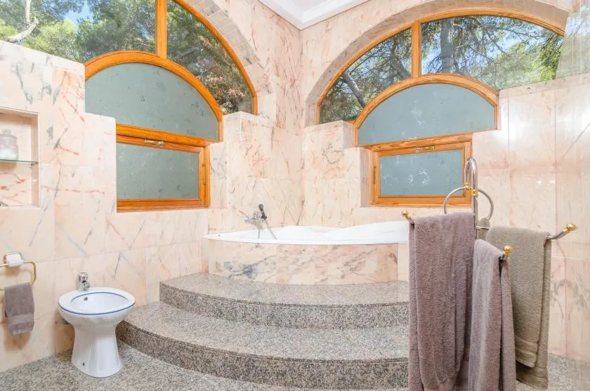 A marble bathroom with a raised bathtub beneath arched windows.