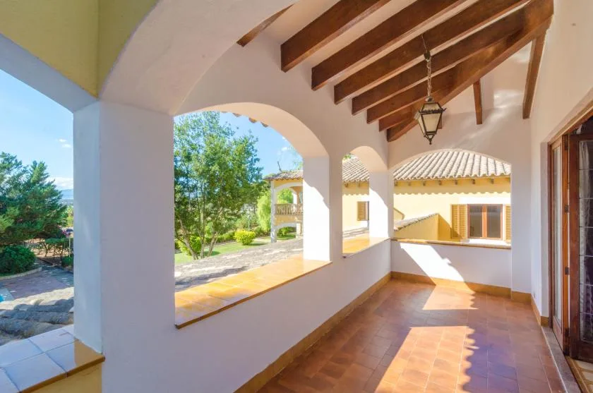 A covered terrace with arched openings, wooden ceiling beams, and a view of the garden.