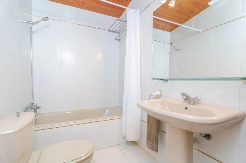 A tiled bathroom with a bathtub, toilet, and sink beneath a wooden ceiling.