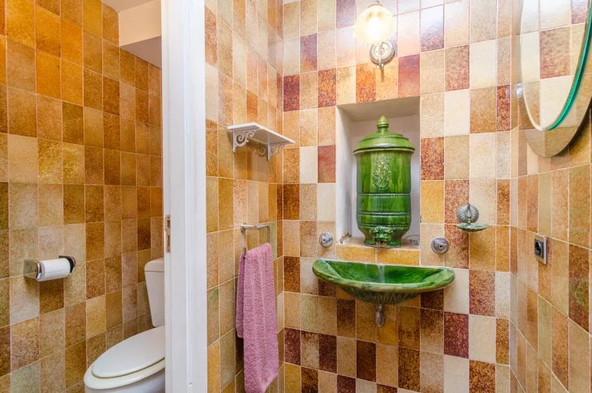 A tiled bathroom with a green basin and a toilet visible behind a partition.