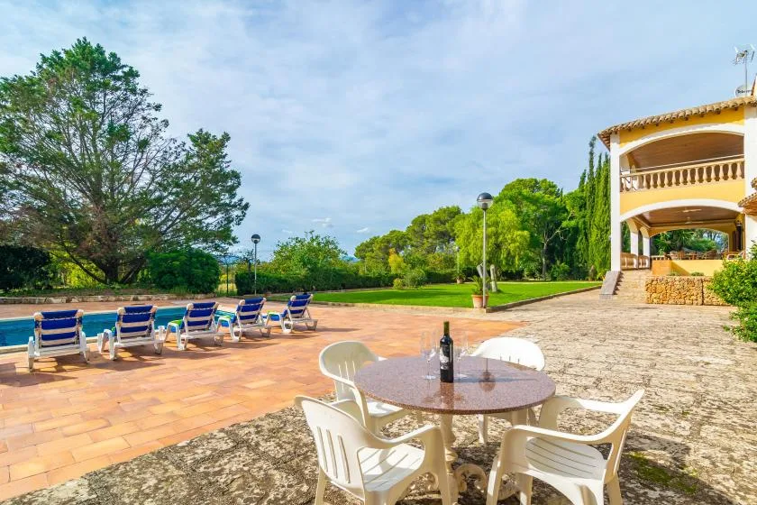 An outdoor patio with a round table and seating overlooks a swimming pool and lawn.