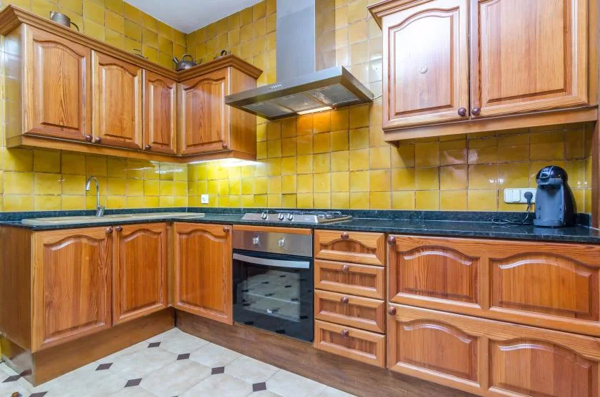 A tiled kitchen with wooden cabinets, a countertop, and a built-in oven.