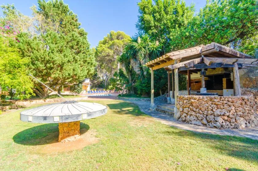 A grassy outdoor area with a round table and a rustic open-sided shelter.