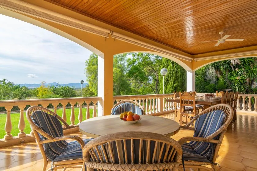 A covered outdoor dining area with a round table and surrounding seating.